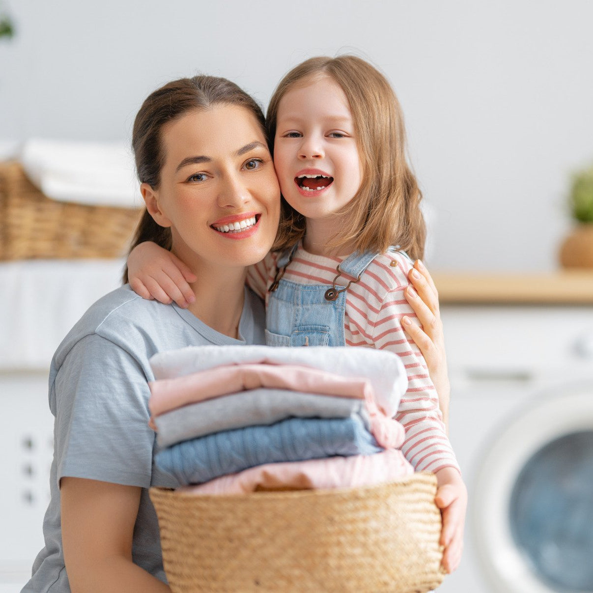 Woman and child holding a basket of laundry in a home setting with a washing machine in the background.