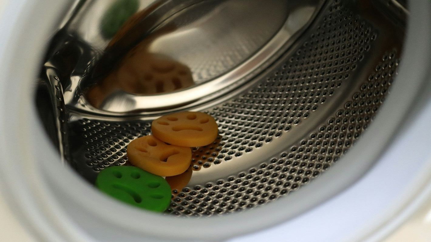 Metal mesh filter with colorful buttons inside a washing machine drum.